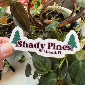 May include: A white sticker with a pink outline featuring the text "Shady Pines Miami, FL" in black with two green pine trees on either side.
