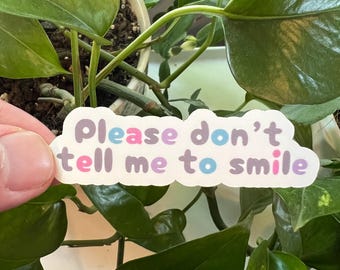 Pode incluir: Um adesivo branco com o texto "Please don't tell me to smile" em uma fonte roxa, rosa e azul.