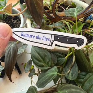 May include: White sticker with a black knife and the text "Beware the Ides" in blue.