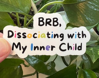 Pode incluir: Etiqueta branca com o texto "BRB, Dissociating with My Inner Child" em preto. As palavras "Dissociating" e "Inner" têm letras coloridas.