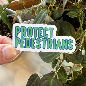 May include: White sticker with blue and green lettering that reads "PROTECT PEDESTRIANS".