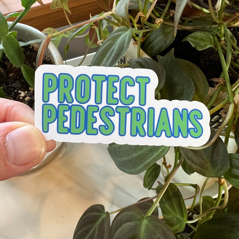 May include: White sticker with blue and green lettering that reads "PROTECT PEDESTRIANS".