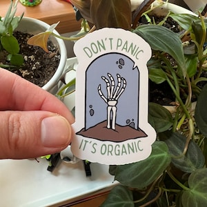 May include: A white sticker with a cartoon skeleton hand emerging from a tombstone. The tombstone is blue and has the text "Don't Panic" on top and "It's Organic" on the bottom.