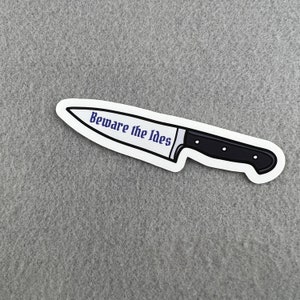 May include: A white sticker with a black knife illustration and the text "Beware the Ides" in purple.