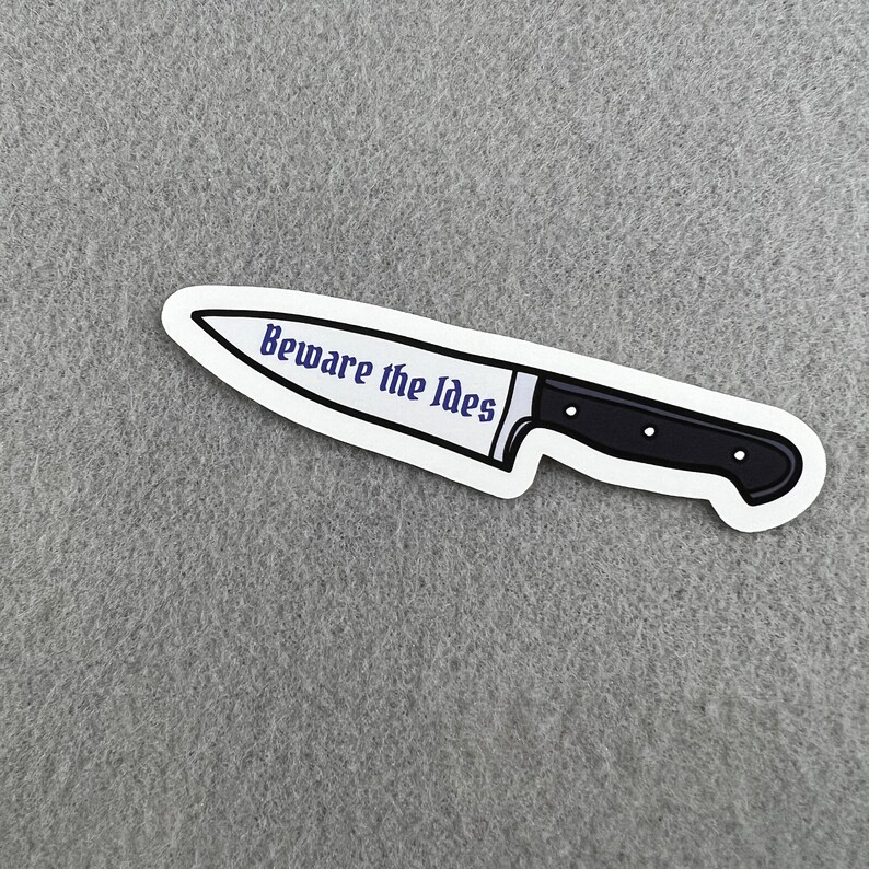 May include: A white sticker with a black knife illustration and the text "Beware the Ides" in purple.