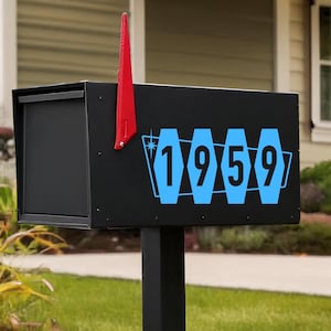 May include: A black mailbox with the number "1959" in blue, set against a green lawn. The mailbox has a red flag and is mounted on a black post. The "Fendershirts Vintage" logo is in the bottom right corner.