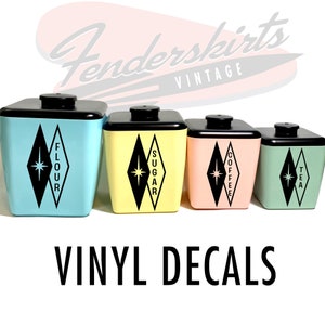 May include: Set of four vintage kitchen canisters with black lids and diamond-shaped decals. The canisters are labeled "Flour", "Sugar", "Coffee", and "Tea". The canisters are in blue, yellow, pink, and green.