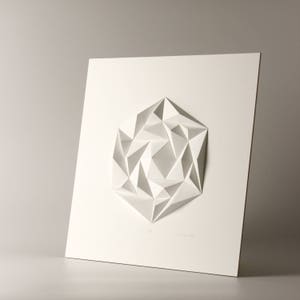 May include: A white paper sculpture of a geometric shape, resembling a flower or a star, mounted on a white background.