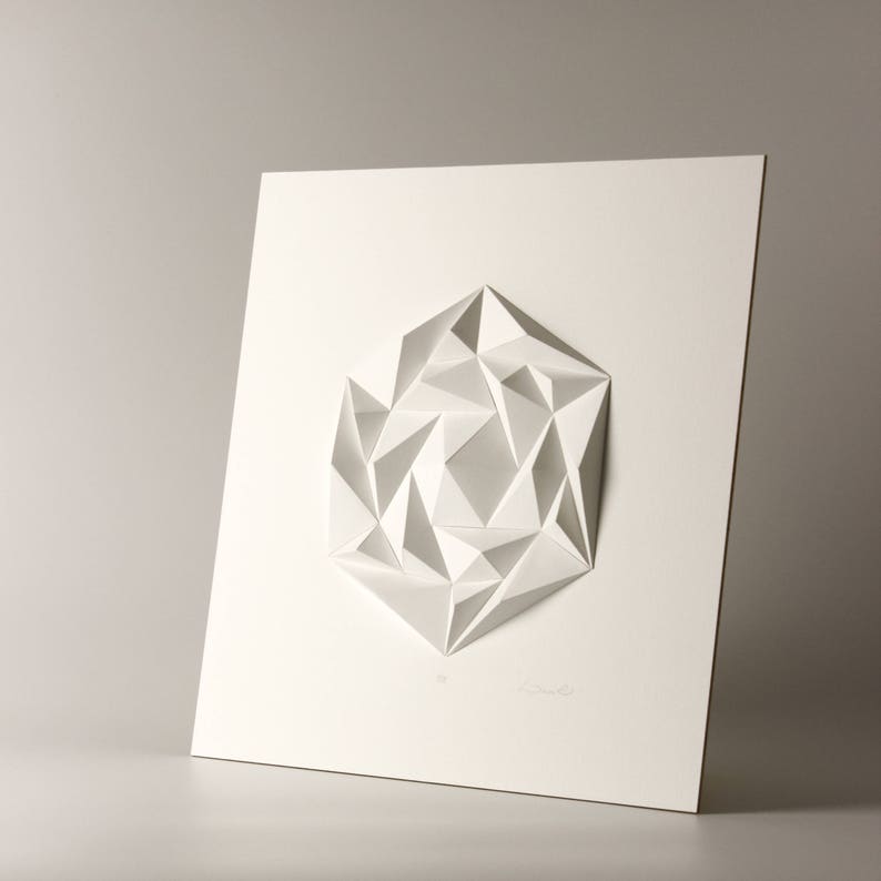 May include: A white paper sculpture of a geometric shape, resembling a flower or a star, mounted on a white background.