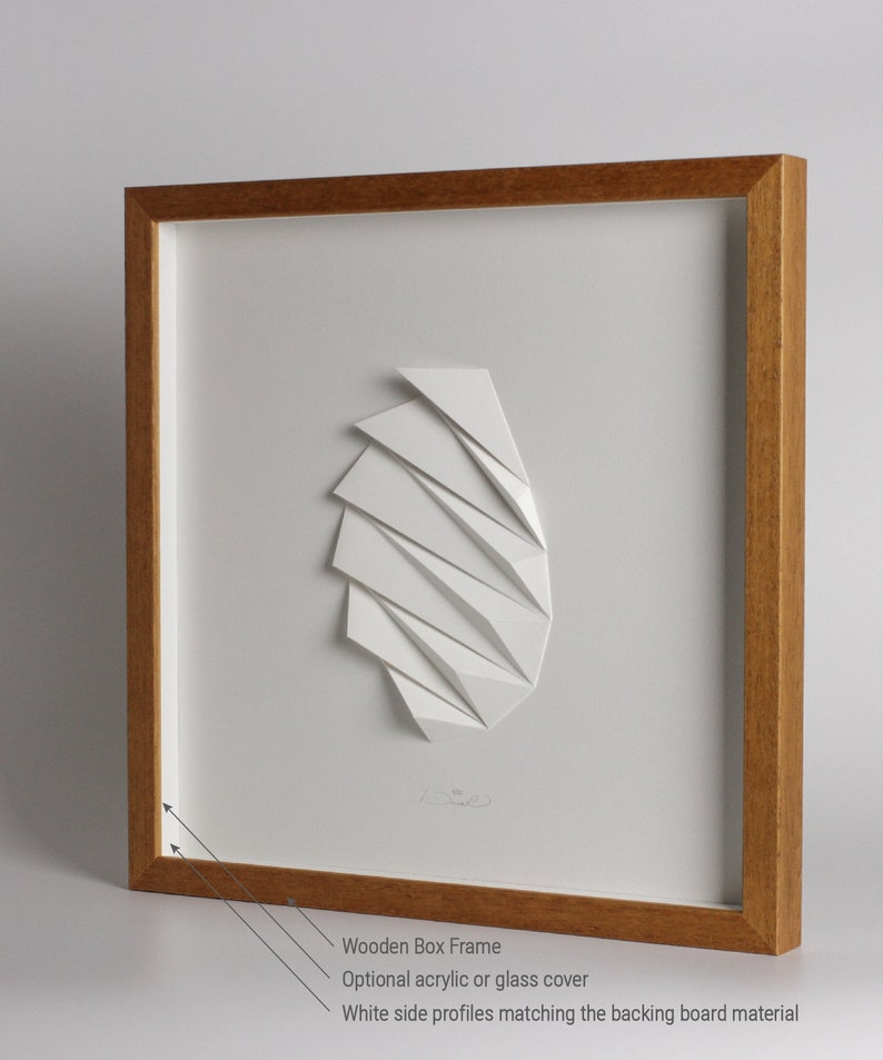 May include: A white paper sculpture of geometric shapes framed in a natural wood box frame. The frame has a white mat and white side profiles.