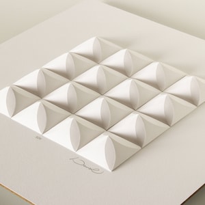 May include: White paper sculpture of a geometric pattern with 16 raised, rounded squares. The sculpture is signed "David" in the bottom right corner.