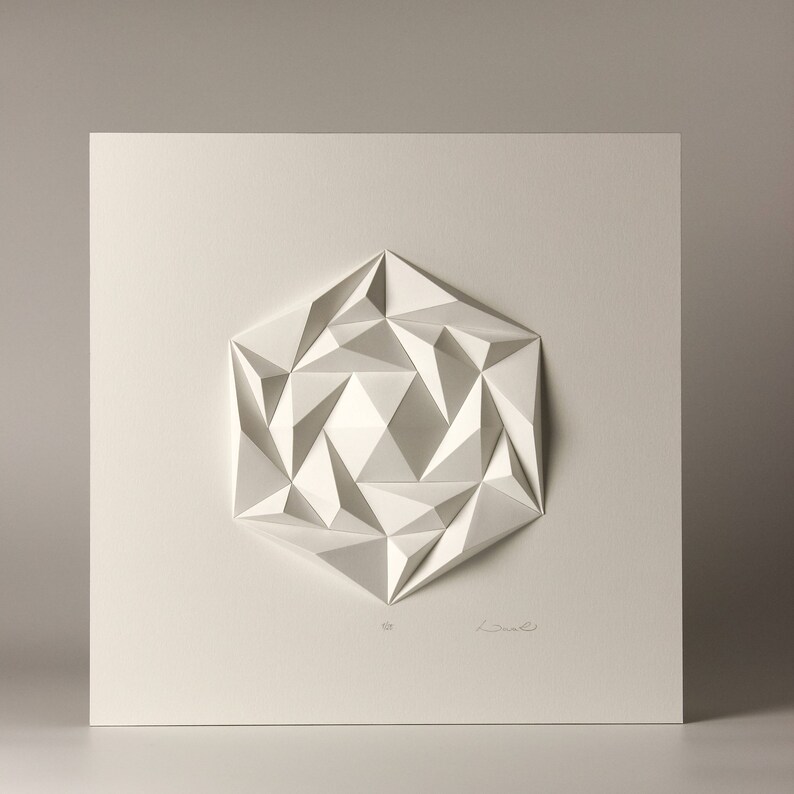 May include: A white paper sculpture of a geometric shape, resembling a flower or star, with a textured, three-dimensional design. The sculpture is mounted on a white background.