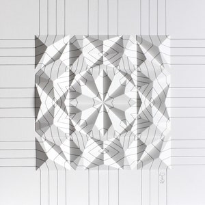 Könnte beinhalten: Eine weiße Papierskulptur mit geometrischem Design. Die Skulptur ist zu einer dreidimensionalen Form mit einem sternförmigen Muster in der Mitte gefaltet. Die Skulptur ist von einem Raster aus schwarzen Linien umgeben.