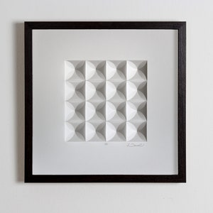 May include: A framed white paper sculpture with a geometric pattern of overlapping circles. The sculpture is signed "Drew" and numbered "4/25".