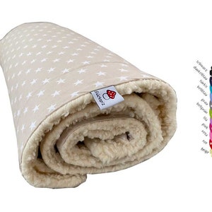 Könnte beinhalten: Eine beige Decke mit weißen Sternen bedruckt. Die Decke ist aufgerollt und hat ein weißes Fleece-Futter. Die Decke hat ein kleines Etikett mit der Aufschrift "Sucker2" und einem roten Pilz-Symbol.
