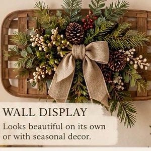 May include: A rectangular woven wooden tobacco basket wall display adorned with green pine branches, pinecones, red berries, and white floral sprigs, centered with a large tan burlap bow. Text reads: WALL DISPLAY Looks beautiful on its own or with seasonal decor.