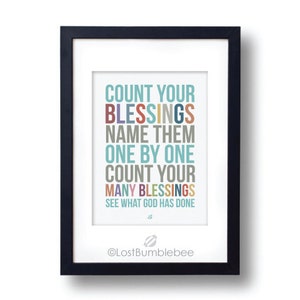 May include: A black framed print with a white background and colorful text that reads "Count your blessings, name them one by one, count your many blessings, see what God has done". The print also includes a small graphic of a planet and the text "@LostBumblebee".