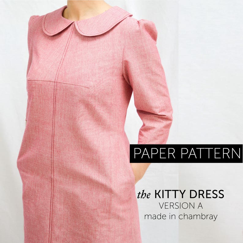 a side view of A woman wearing a red winter dress with 3/4 length sleeves with gathering, round collar, and her hand is in her pocket. The dress has interesting bust dart details and topstitching.
