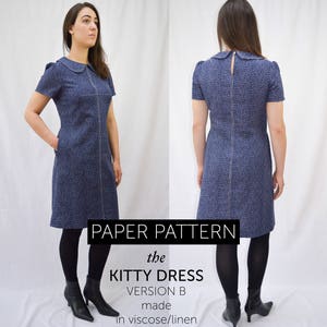 A woman wearing a blue and white spot winter dress or fall dress with short sleeves, Peter pan collar, and her hand is in her pocket. The dress has interesting bust dart details and topstitching.