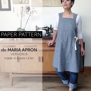 Maria Apron sewing pattern - crossback, Japanese style Studio Makers apron, gardener or kitchen apron in chambray denim worn over jeans in front of an vintage ercol side board