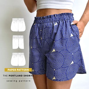 May include: Blue and cream shorts featuring a circular geometric pattern, an elasticized waistband, and side pockets. The image includes a white technical line drawing of the shorts and the text PAPER PATTERN THE PORTLAND SHORTS sewing pattern.
