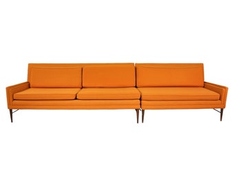 May include: A long, orange, three-piece sectional sofa with wooden legs.