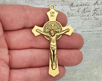 May include: Gold-toned metal crucifix with a depiction of Jesus Christ on the cross. The crucifix has a circular halo around the head of Jesus with the inscription "IN RI" on the top of the cross.