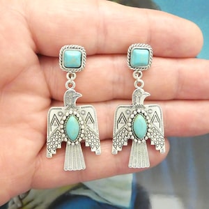 May include: A pair of silver dangle earrings with turquoise stones. The earrings feature a stylized bird design with intricate details.