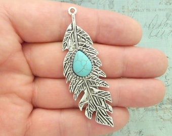 May include: Silver feather charm with a turquoise stone. The feather has a detailed design and a loop at the top for attaching to jewelry.