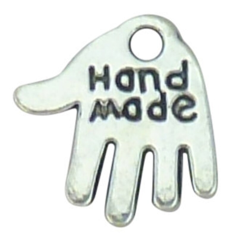 May include: A silver-coloured charm shaped like a hand, with the words "HAND MADE" in capital letters. It features a small hole at the top for attaching to jewellery. The charm is likely made of metal and is suitable for crafting.