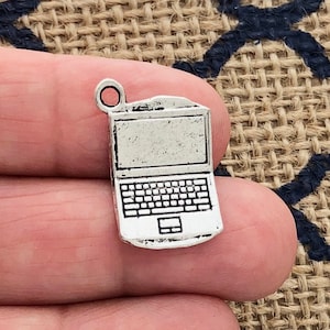 May include: A silver-colored laptop charm with a detailed keyboard and screen. The charm has a small loop at the top for attaching to a necklace or bracelet. The laptop charm is made of metal and has a slightly distressed finish.