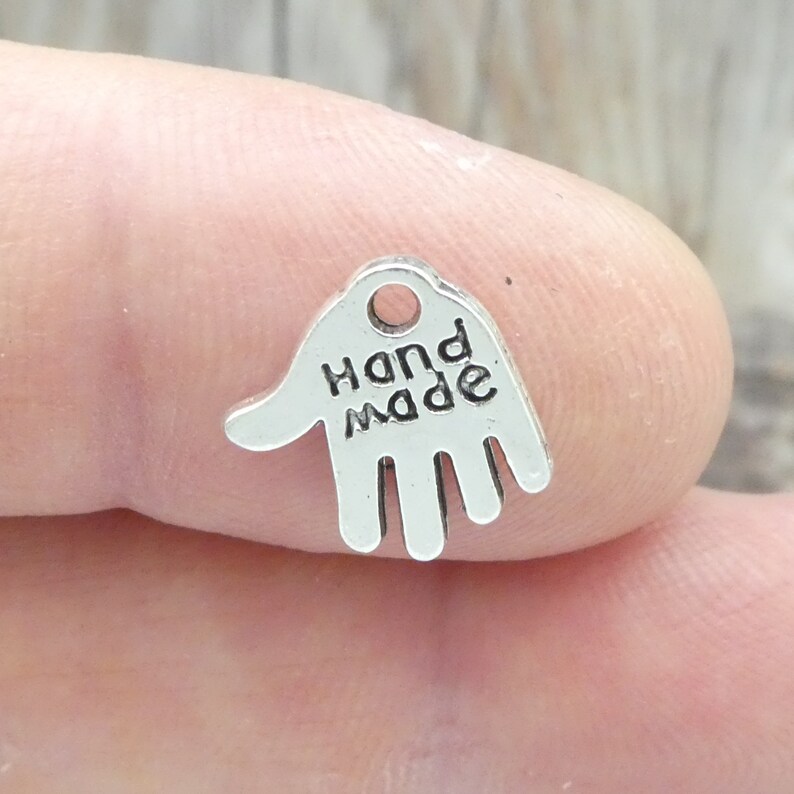 Puede incluir: Encanto de plata en forma de mano con la palabra "Handmade" inscrita en &eacute;l.