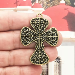 May include: A gold-toned metal cross pendant with an intricate, filigree design. The cross has a four-leaf clover shape with a central cross.