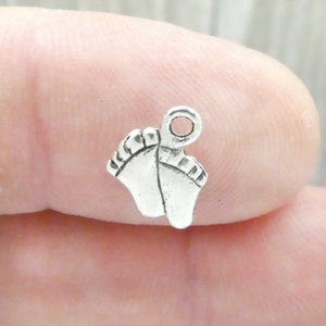 May include: Silver charm in the shape of two baby footprints with a loop for attaching to a necklace or bracelet.