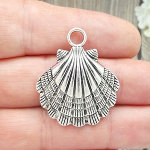 May include: Silver-toned metal seashell charm with a loop at the top for attaching to jewelry or crafts.