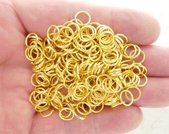 May include: A large pile of gold jump rings. The rings are all the same size and are arranged in a random pattern.