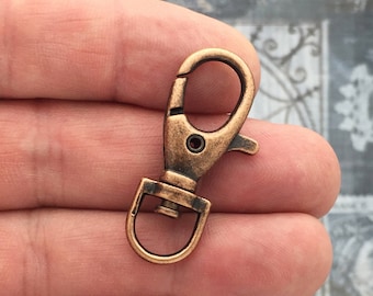 May include: A copper-toned metal swivel clasp with a spring-loaded gate. The clasp is designed for attaching to keychains, bags, or other items.