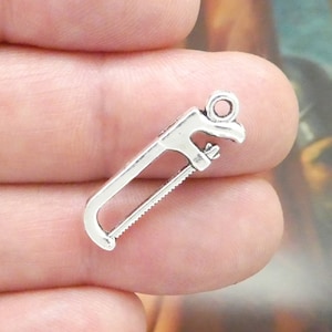 May include: Silver charm in the shape of a hand saw. The charm has a loop at the top for attaching to a necklace or bracelet.