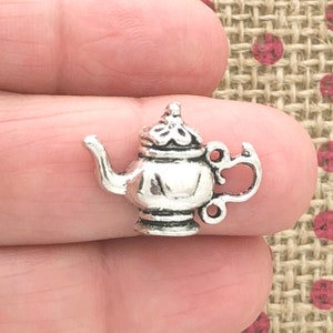 May include: Silver teapot charm with a detailed design. The charm has a spout, handle, and lid. It is a great addition to jewelry making or scrapbooking.