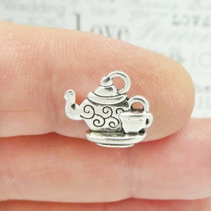 May include: Silver charm in the shape of a teapot and cup. The teapot has a swirl design and the cup has a handle. The charm is on a white background.