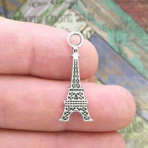 May include: Silver charm in the shape of the Eiffel Tower. The charm has a loop at the top for attaching to a necklace or bracelet.