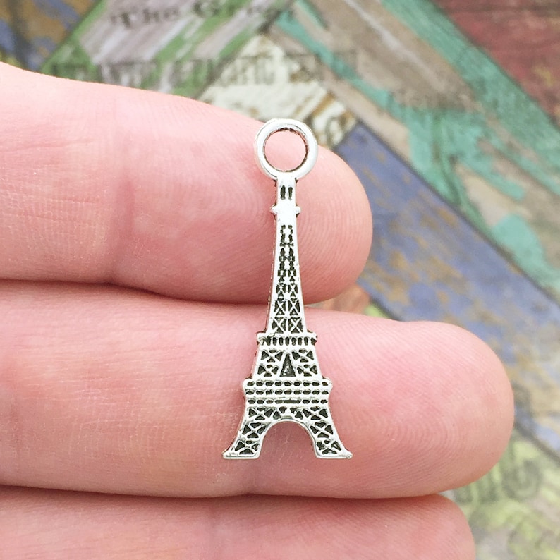 May include: Silver charm in the shape of the Eiffel Tower. The charm has a loop at the top for attaching to a necklace or bracelet.