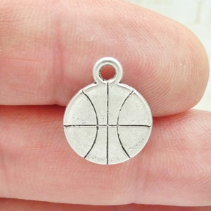 May include: Silver charm in the shape of a basketball. The charm has a loop at the top for attaching to a necklace or bracelet.