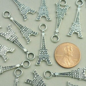 May include: Silver charm pendants in the shape of the Eiffel Tower. Each charm has a small loop at the top for attaching to a bracelet or necklace.