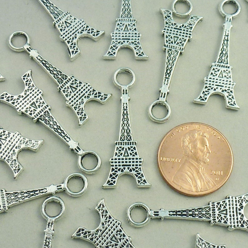 May include: Silver charm pendants in the shape of the Eiffel Tower. Each charm has a small loop at the top for attaching to a bracelet or necklace.