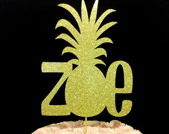 Puede incluir: Topper de pastel de piña con purpurina dorada con el nombre "Zoe" en un pastel glaseado de color rosa.