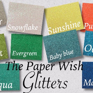 May include: A collection of glitter samples in various colours, including silver, snowflake, sunshine, pumpkin, cricket, evergreen, baby blue, ocean, aqua, and marine. The text "The Paper Wish Glitters" is displayed below the samples.