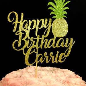 May include: Gold glitter cake topper with the words "Happy Birthday Carrie" and a green glitter pineapple.