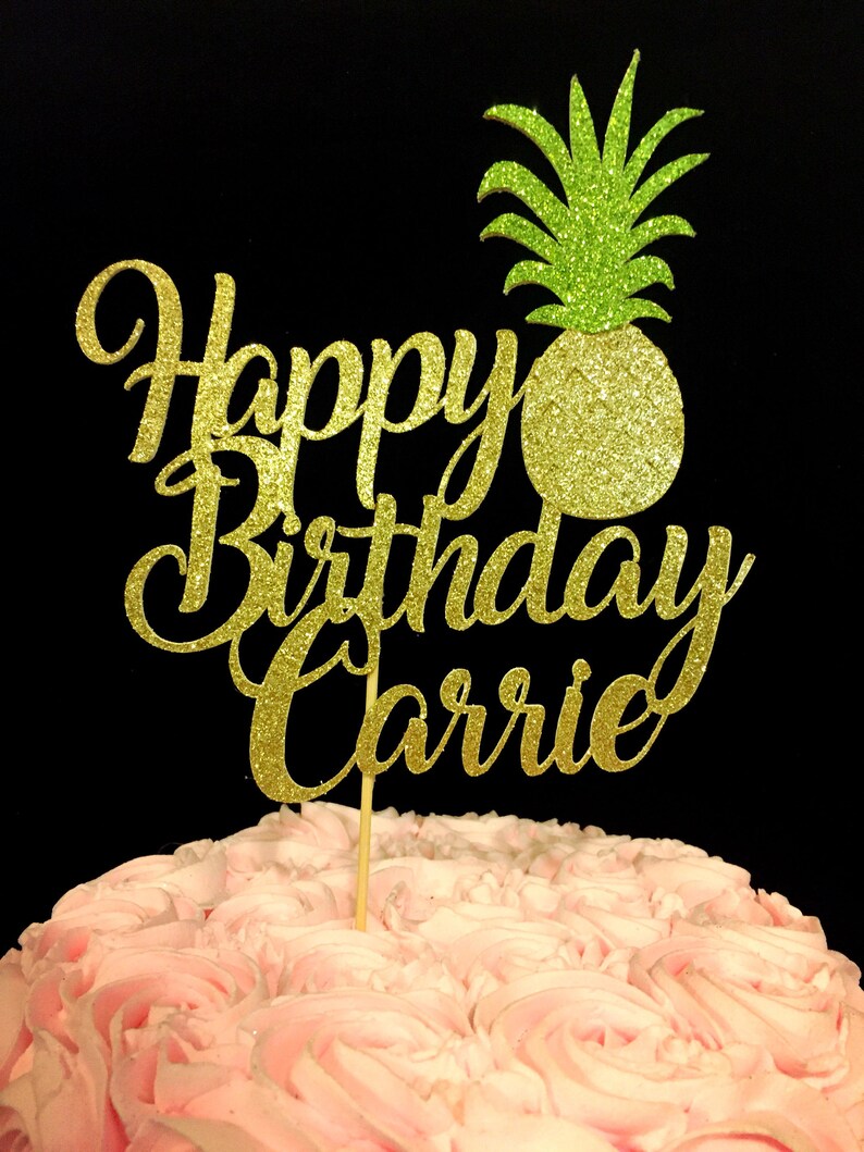May include: Gold glitter cake topper with the words "Happy Birthday Carrie" and a green glitter pineapple.