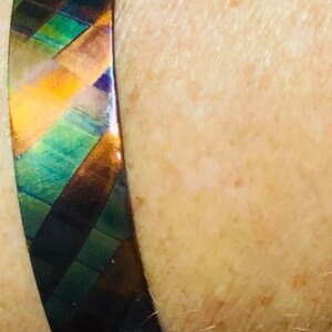 May include: A copper bracelet with a geometric pattern in shades of green, blue, and orange.